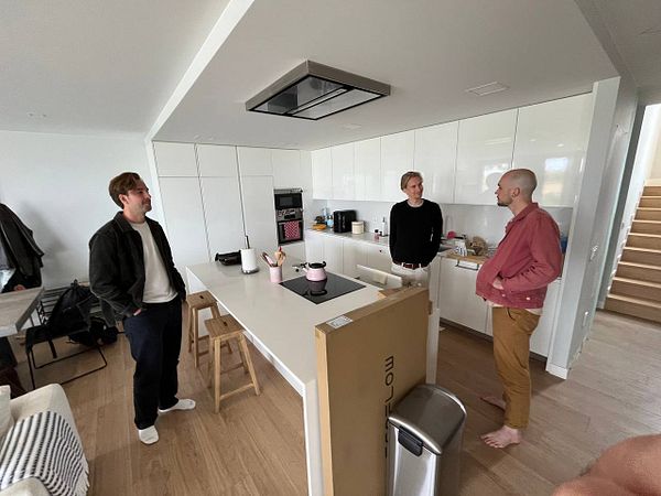 Three men are engaged in conversation in a modern kitchen space.