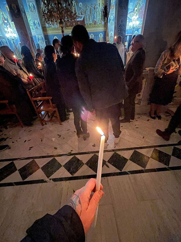 A person holds a lit candle in a dimly lit church filled with worshippers.