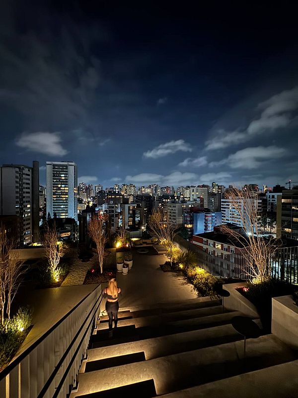 A woman walks down illuminated steps overlooking a vibrant city skyline at night.