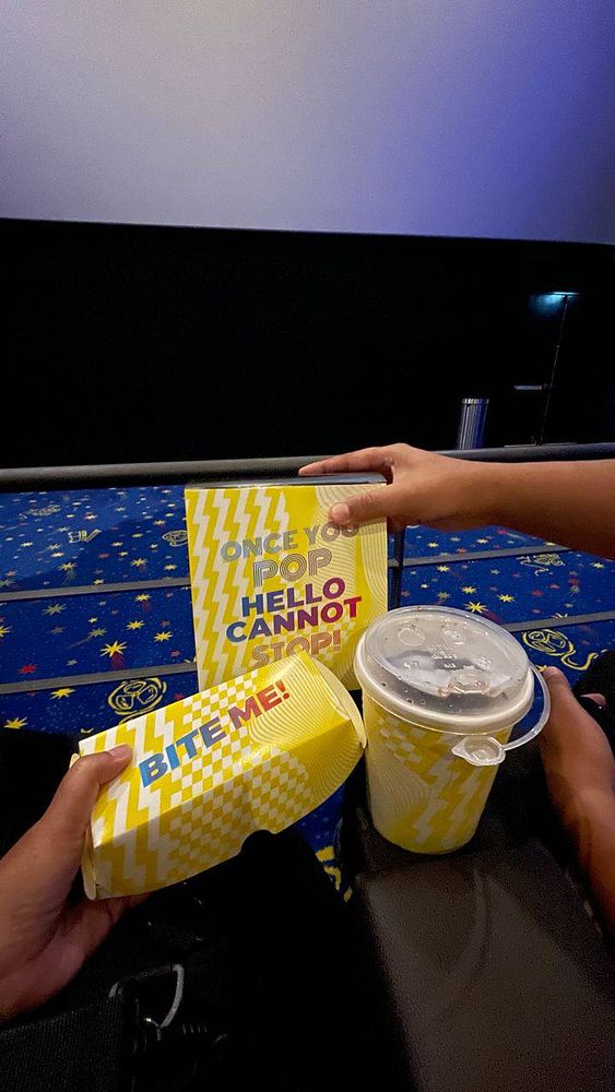 A person is holding popcorn and a drink in a movie theater setting.