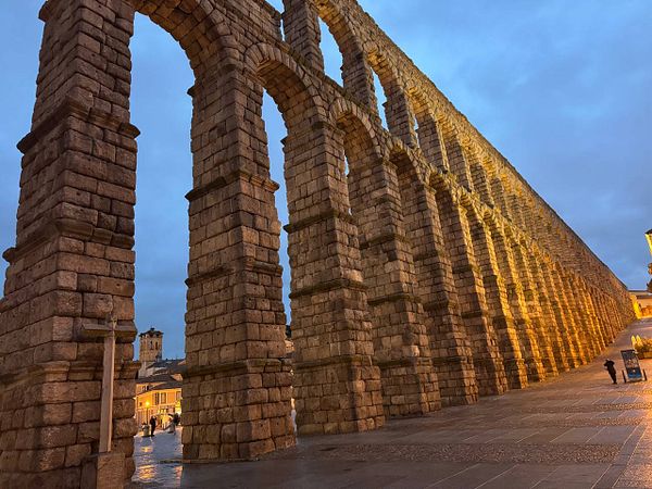 A scenic view of Segovia featuring the iconic Roman aqueduct and historic buildings under a cloudy sky.