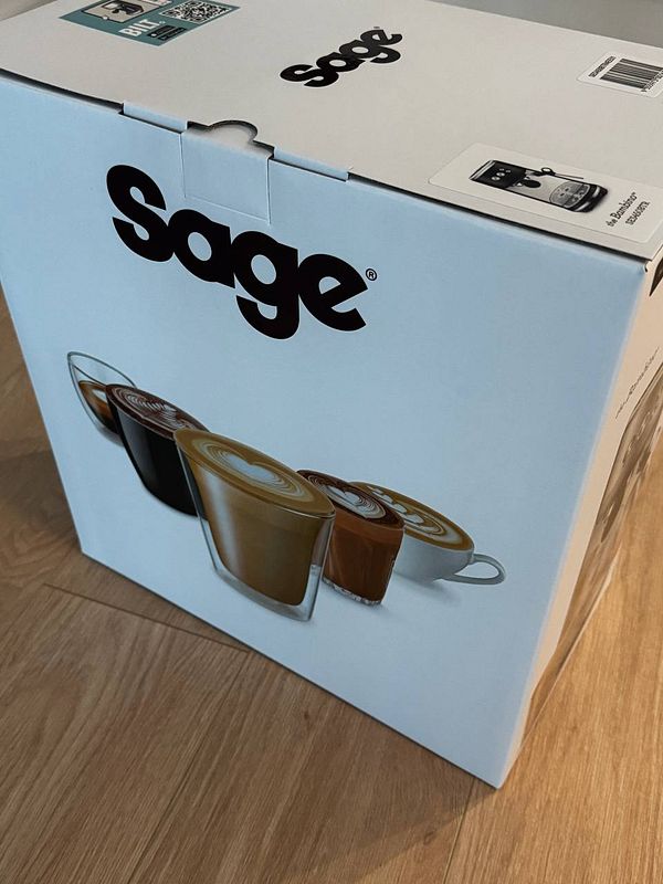 A sleek, modern espresso machine with a digital display and dual spouts, accompanied by a glass of espresso on a kitchen countertop.