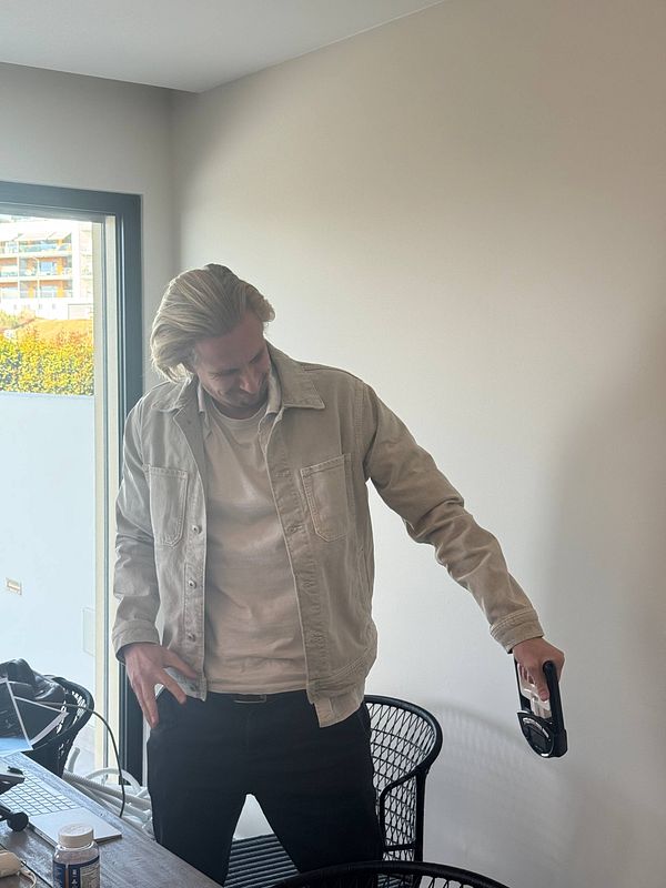 A man stands in a bright, modern workspace, holding a device while looking down.