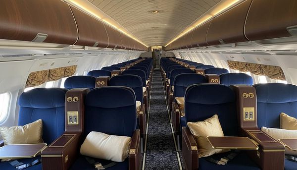 The image depicts the interior of an airplane cabin featuring rows of plush blue seats.