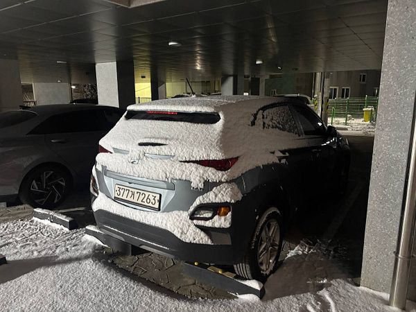 A car covered in snow is parked in a dimly lit underground parking garage.