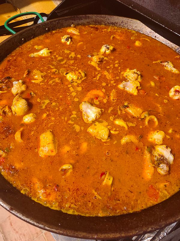 A homemade paella dish served on a table with a morning beach view in the background.