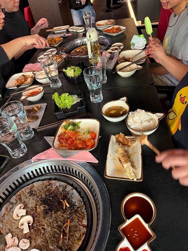 A wooden tray holds an assortment of raw meats and a bowl of green soup for Korean BBQ.