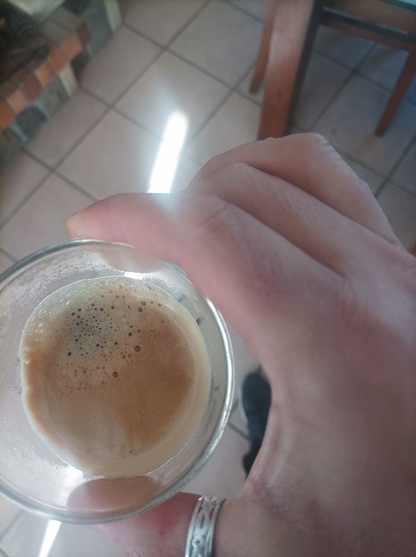 A hand holding a glass of espresso with a cozy indoor background.