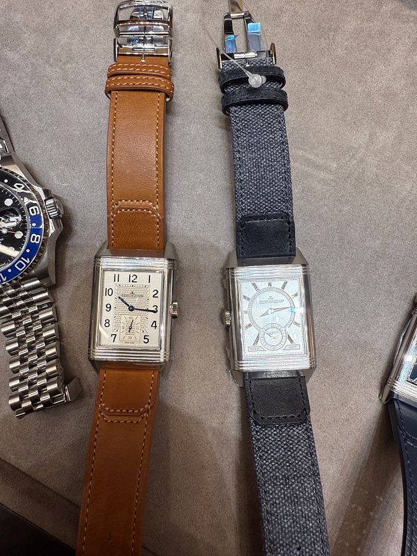 The image features two luxury watches displayed side by side on a soft surface.