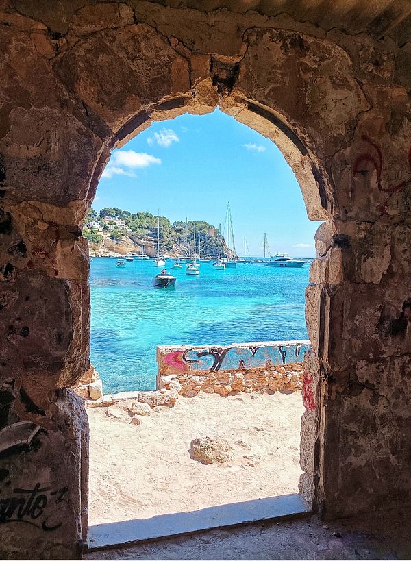 A picturesque view of a beach framed by an arched stone doorway.