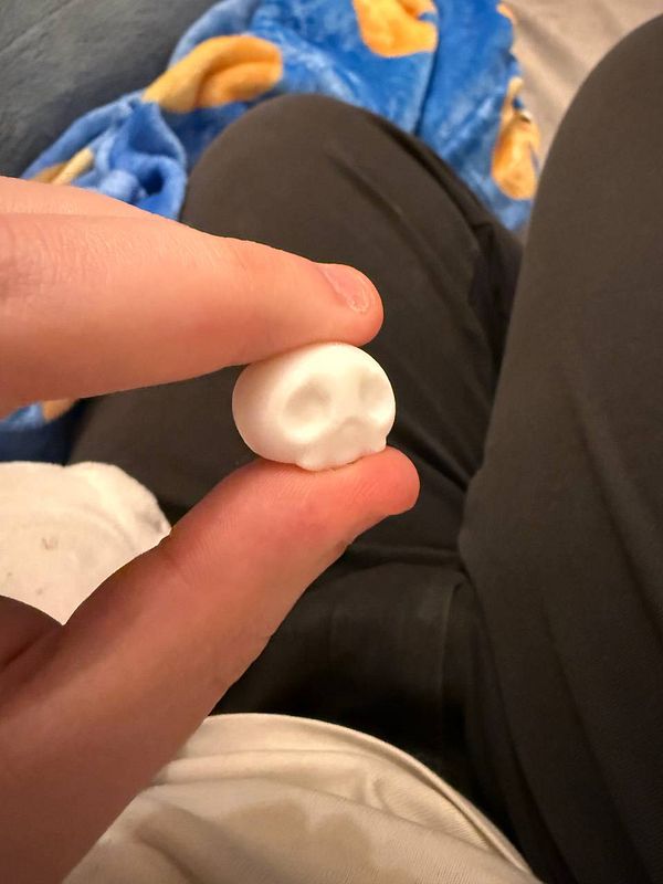 A small white skull design is being held between a person's thumb and index finger.