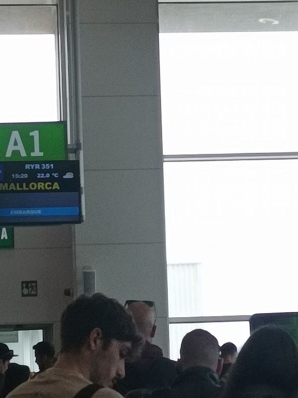 The image captures a busy airport boarding area with a flight information display.