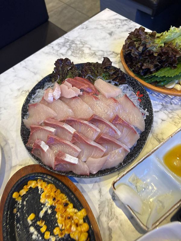 A beautifully arranged platter of sashimi featuring Japanese amberjack, accompanied by various side dishes.