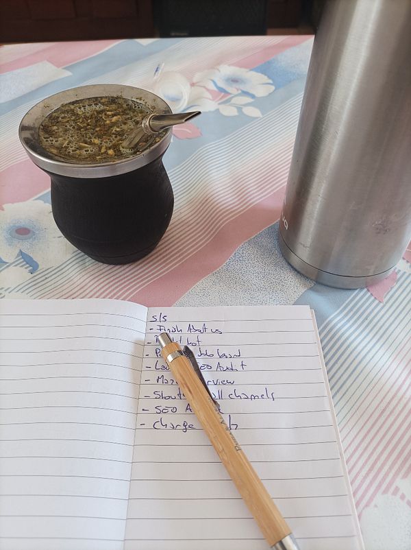 A cozy workspace featuring a traditional mate drink, a notebook with tasks, and a thermos.