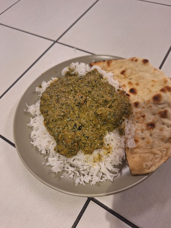 A plate of Indian food featuring rice, a green curry, and naan bread.