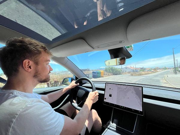 A young man is driving a car on a sunny road with a digital display in front of him.