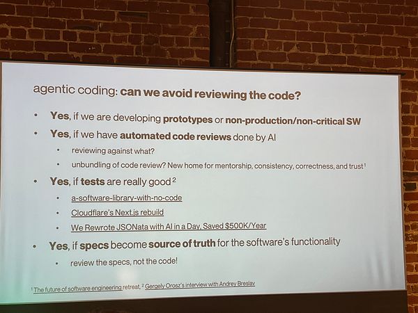 A photograph of a casual indoor meetup showing four people sitting at a table with food and drinks, engaging in conversation and looking at a laptop.