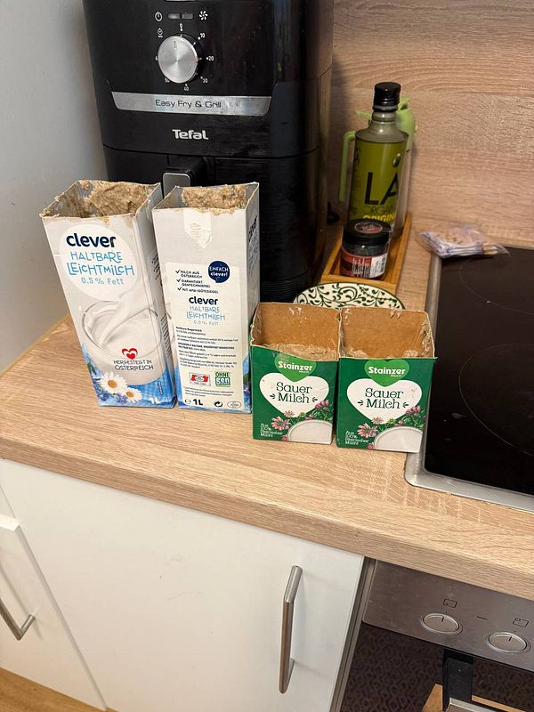 The image features a kitchen countertop with various empty milk cartons and a kitchen appliance.
