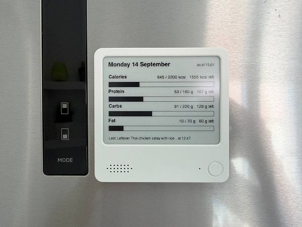 A ZecTrix e-ink device attached to a refrigerator displaying a user interface for macros tracking.