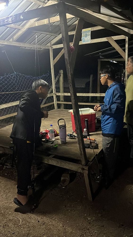 A group of individuals is preparing for a fishing trip at a wooden shelter at night.