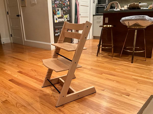 A vintage wooden child's chair with a blue painted seat and backrest, showing signs of wear and tear, set against a wooden wall.