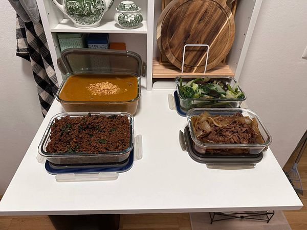 Four meal prep containers filled with different dishes are arranged on a table.