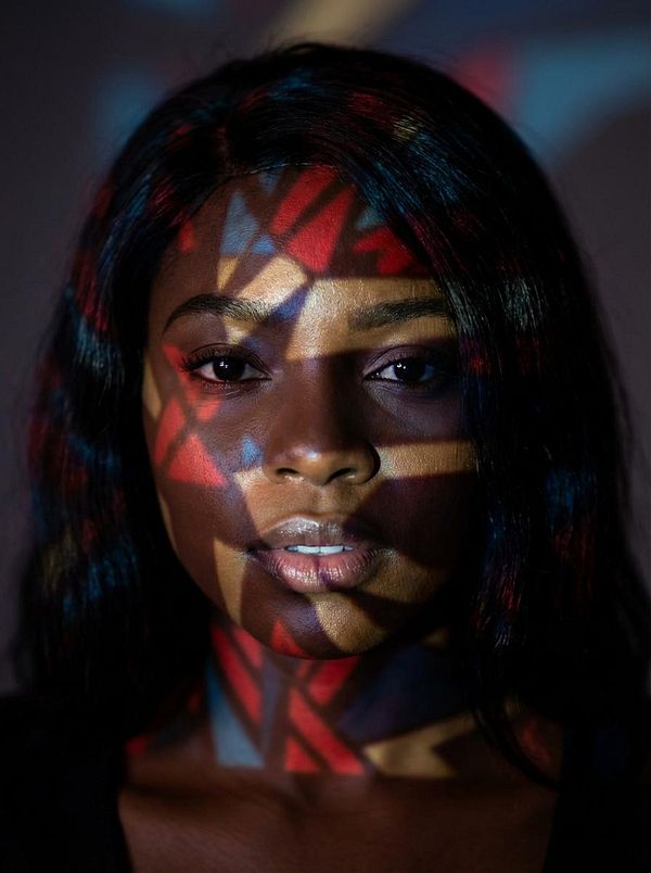 A close-up portrait of a woman with colorful light patterns projected onto her face.