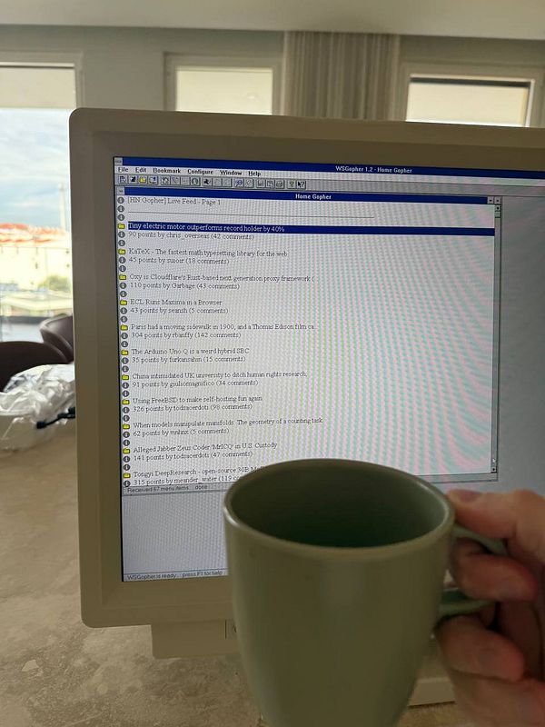 A person is holding a coffee cup in front of a computer screen displaying Hacker News content.