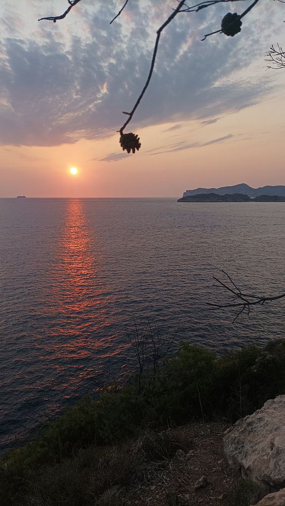 A serene sunset over the ocean with a rocky coastline in the background.