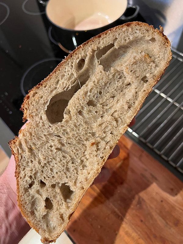 A freshly baked sourdough loaf is being held, showcasing its interior texture.