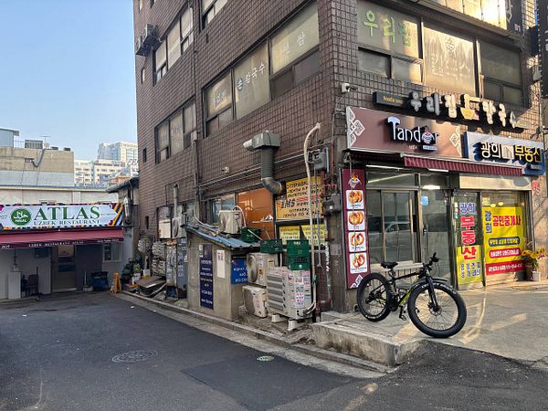 A street view of a Soviet-style residential neighborhood in Seoul featuring mid-rise apartment buildings and colorful signage.