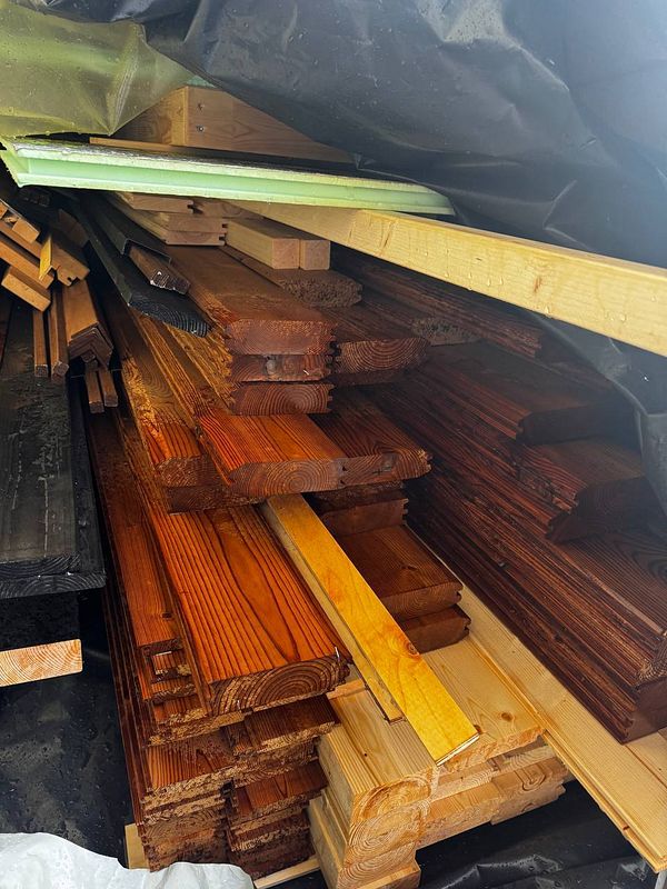 A stack of wooden planks is shown, partially covered and wet from rain.