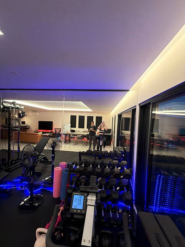 A gym scene showing two individuals exercising with dumbbells inside a workout room with various fitness equipment.