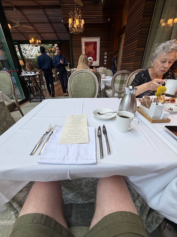 A warm, intimate photo of an elderly woman smiling beside a cup of coffee and a bowl of food at a wooden table.