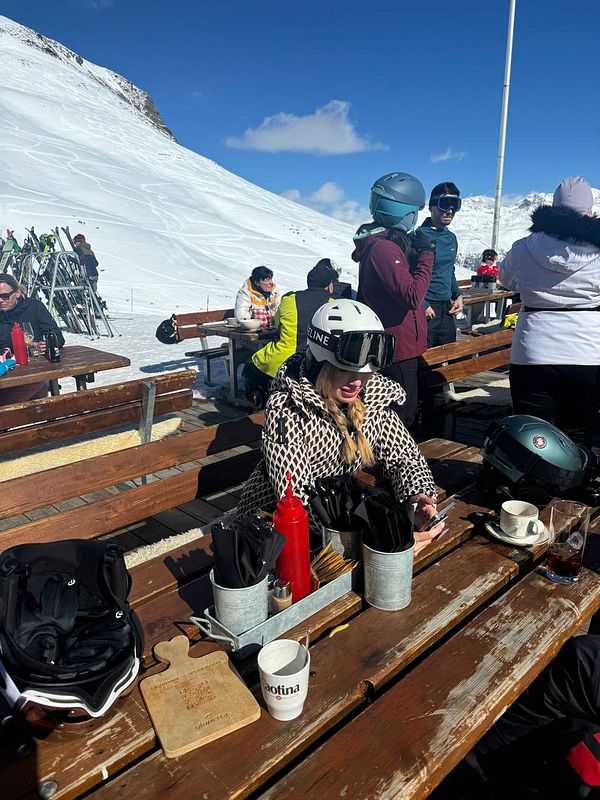 A woman in ski gear enjoys a break at a snowy mountain restaurant.