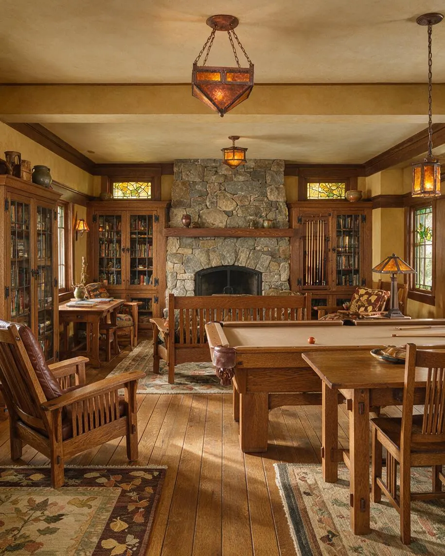 A Craftsman-style game room with a large central stone fireplace, built-in wood cabinets with glass doors, and a pool table in the foreground. The room features warm wood trim, paneled ceilings, amber stained-glass pendant lights, patterned rugs, and leather and wood seating arranged around the space.