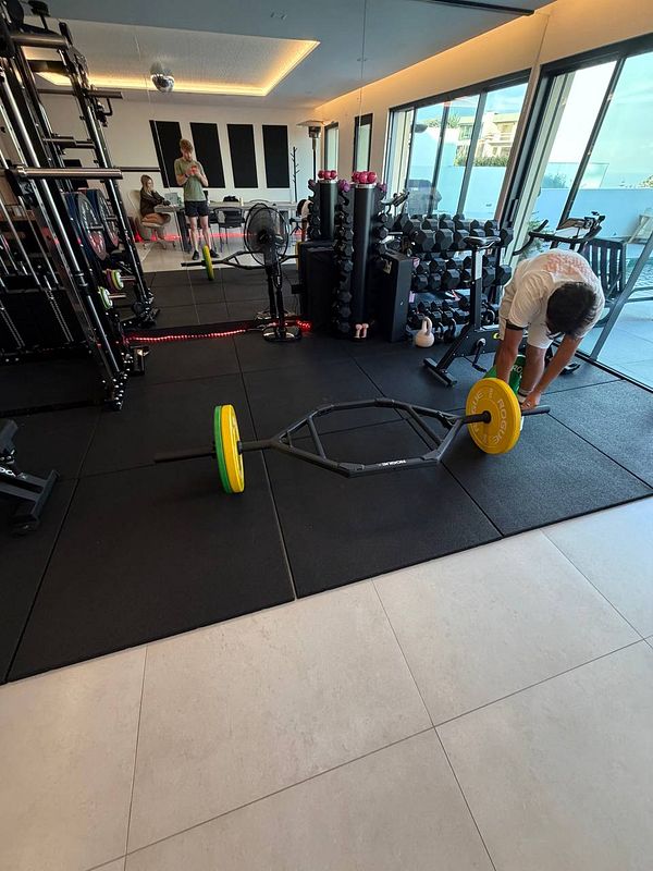 A man in a modern home gym setting is preparing weights on a hex bar for lifting.