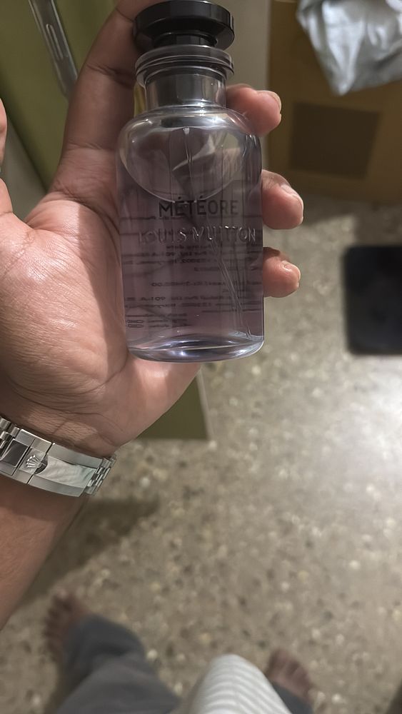 A person holds a bottle of Louis Vuitton's cologne, Meteore, in a domestic setting.