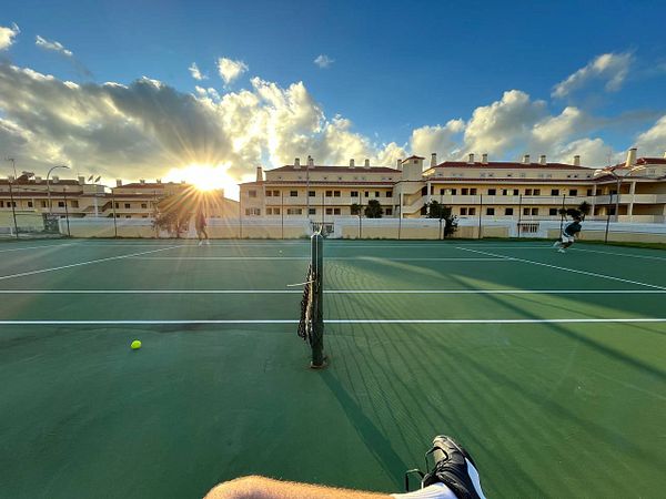 A tennis court at sunset with players engaged in a game.