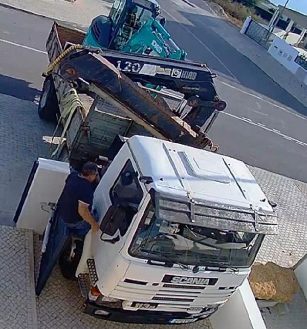 A truck driver is seen interacting with a large white Scania truck parked near a residential area.