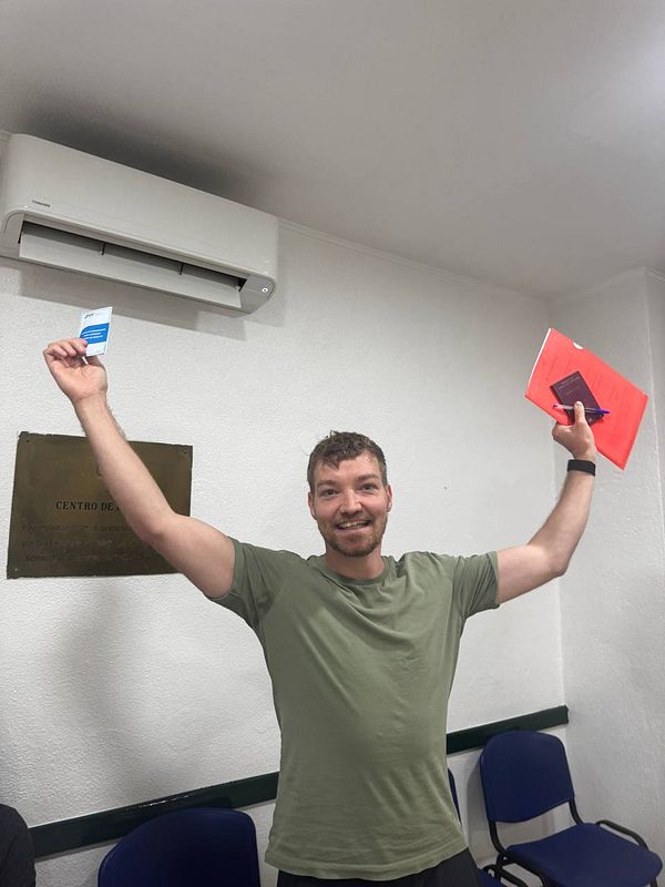 A man celebrates after passing his theory driving test, holding up his test results and a notebook.