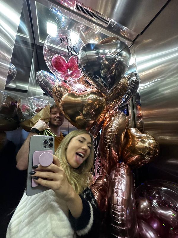 A joyful moment captured in an elevator filled with balloons and a couple celebrating a birthday surprise.