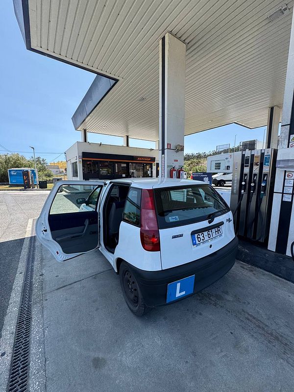 A white car with a learner's plate is parked at a gas station with its door open.