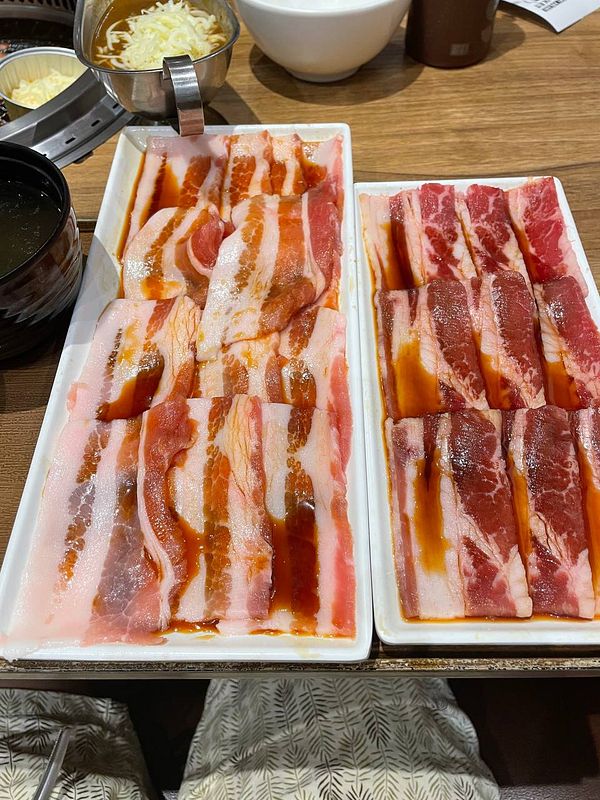 A grill at a yakiniku restaurant with pieces of meat and vegetables cooking on the mesh grill over hot coals.